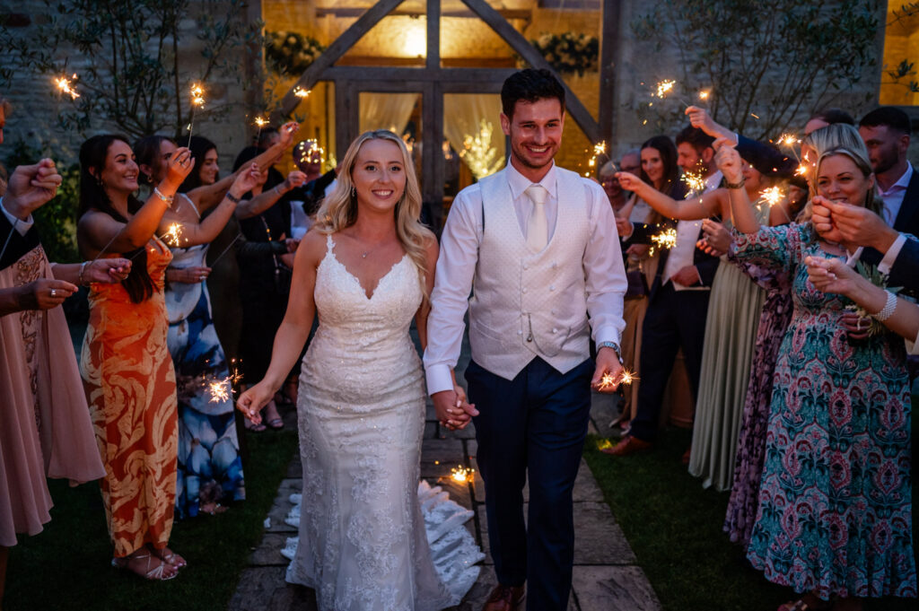 bride and groom surrounded by guests with sparklers in late evening time