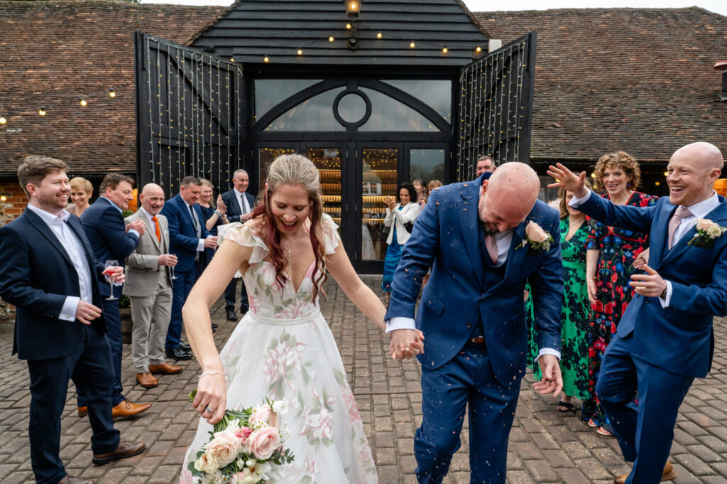 Kristin and Simon laughing and dodging confetti during their unexpected confetti moment at Old Luxters Barn micro-wedding elopement.
