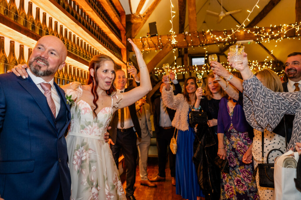 Candid reactions of friends and family during toasts and cake cutting at Kristin and Simon’s micro-wedding elopement in the barn at Old Luxters Barn