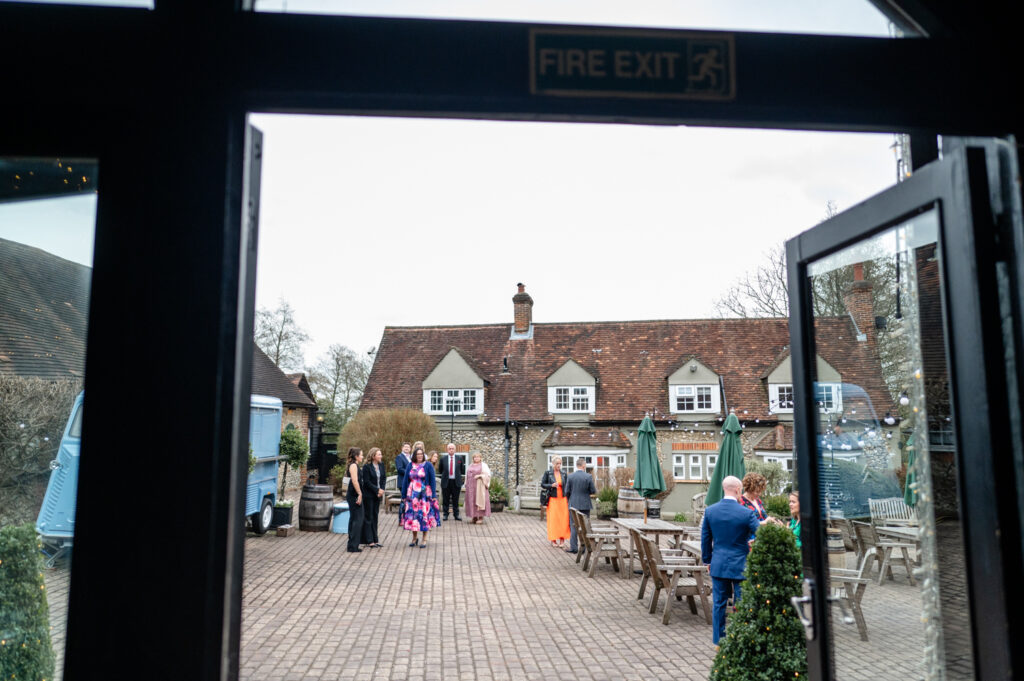 Guests gathering in the courtyard at Old Luxters Barn before Kristin and Simon’s micro-wedding elopement, enjoying the relaxed atmosphere and rustic surroundings.