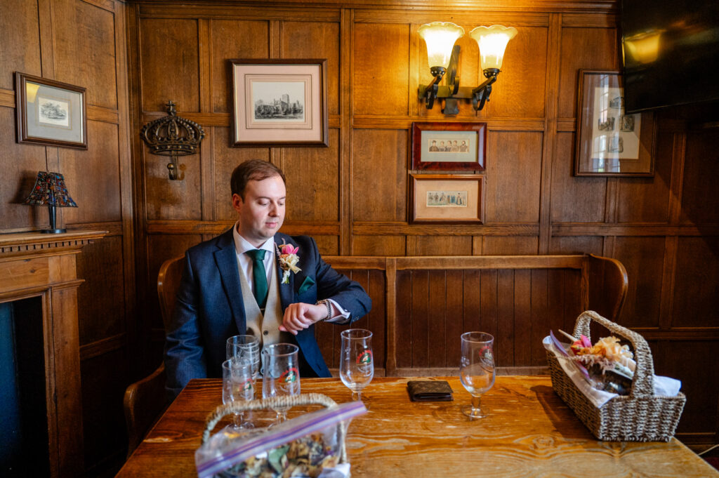 Groom checking his watch while enjoying a drink at the pub before his St Albans Cathedral wedding