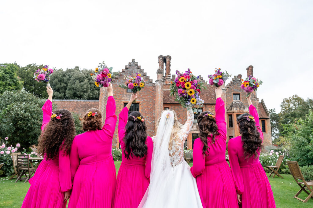Bridesmaids cheer in the gardens at Chenies Manor for wedding photos